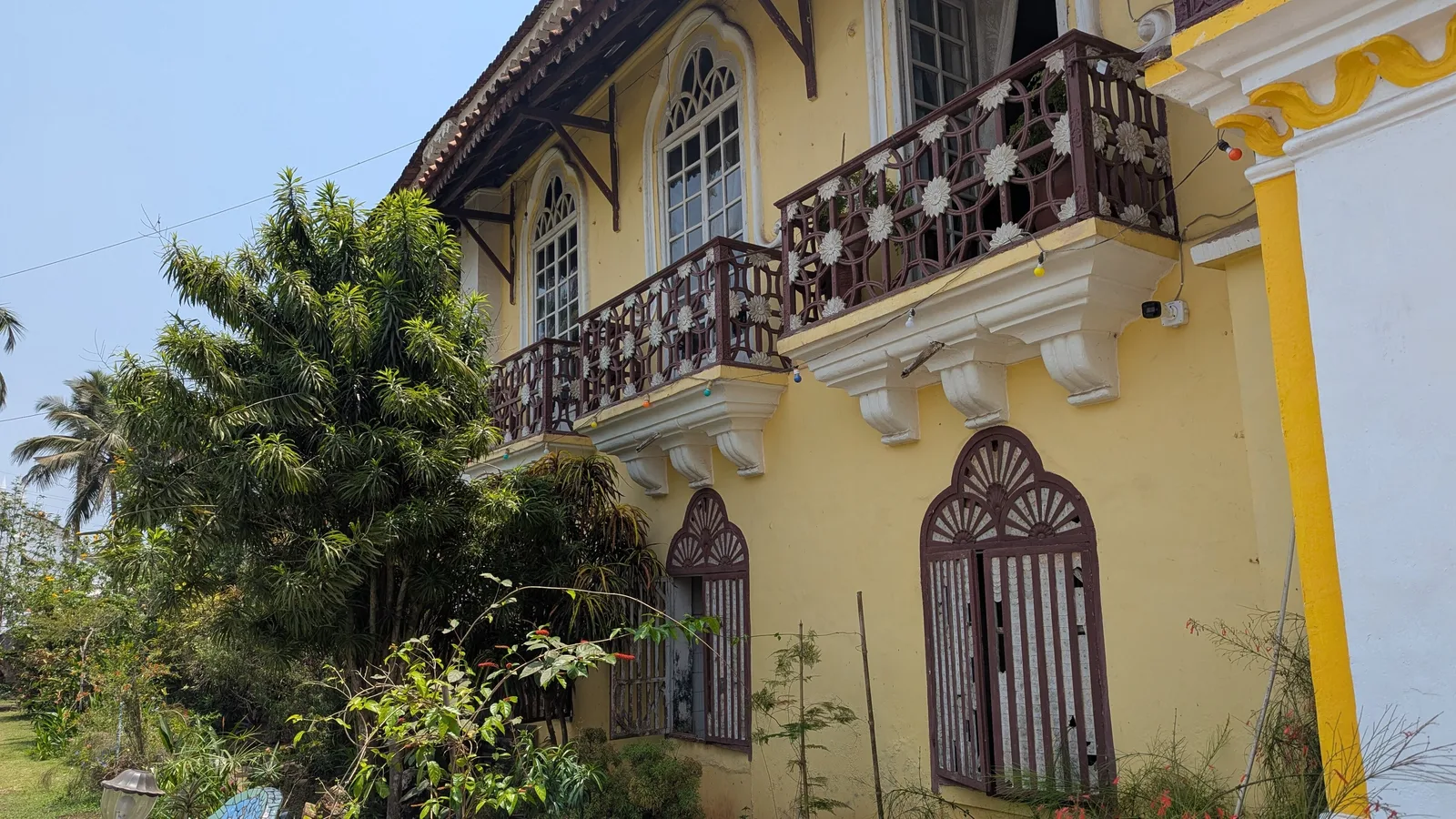 Tall arched windows with carved shell-motif balconies and fan-topped shutters on the yellow Braganza house, Chandor