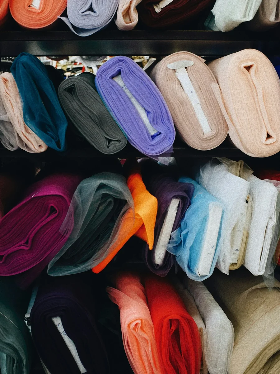 Rolls of fabric in many colours, from sheer tulle to solid weaves, stacked on shop shelves
