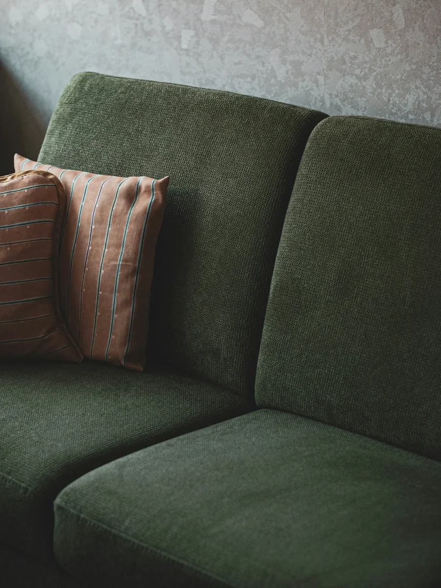 A deep-green textured fabric sofa with soft back cushions and two striped scatter cushions