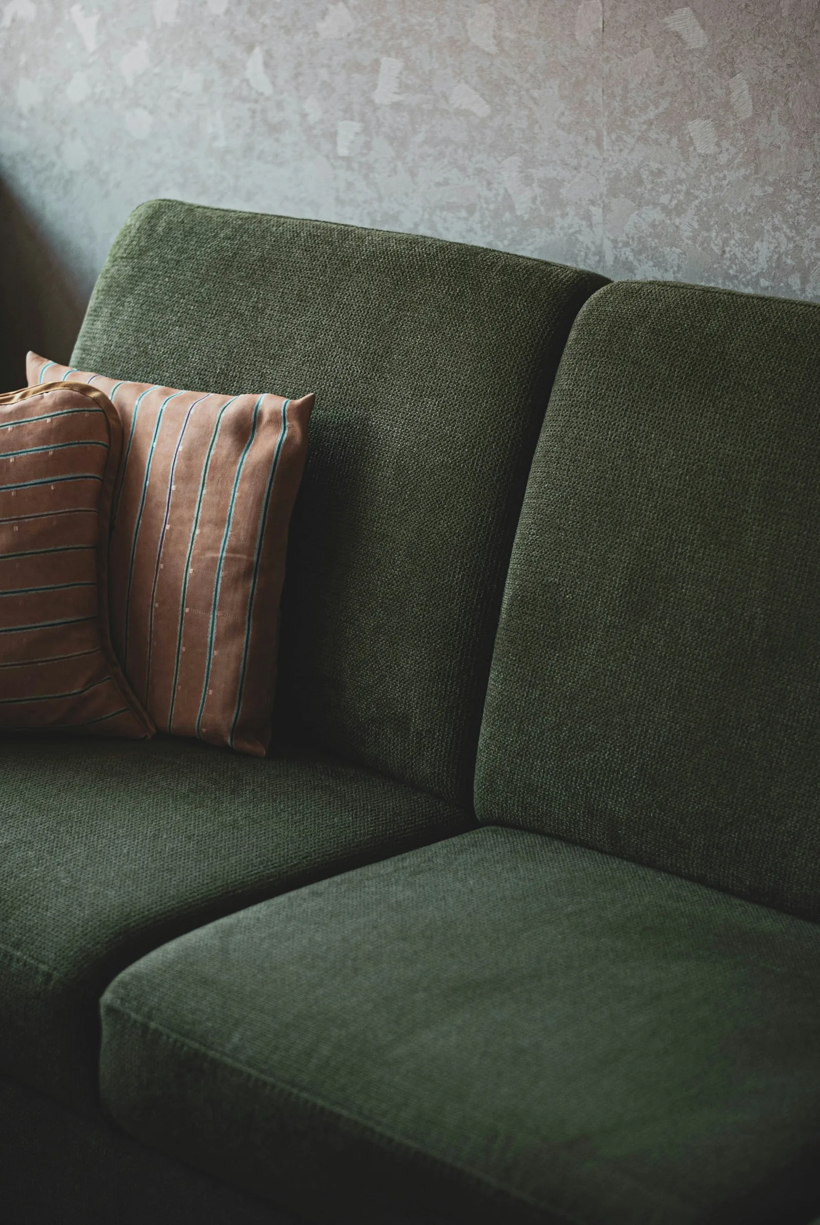 A deep-green textured fabric sofa with soft back cushions and two striped scatter cushions