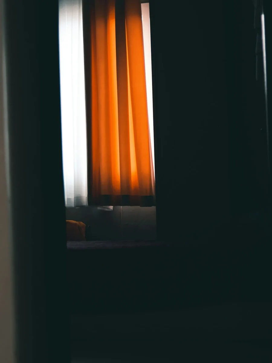 A burnt-orange curtain lit from behind by daylight in an otherwise dark, deep-green room