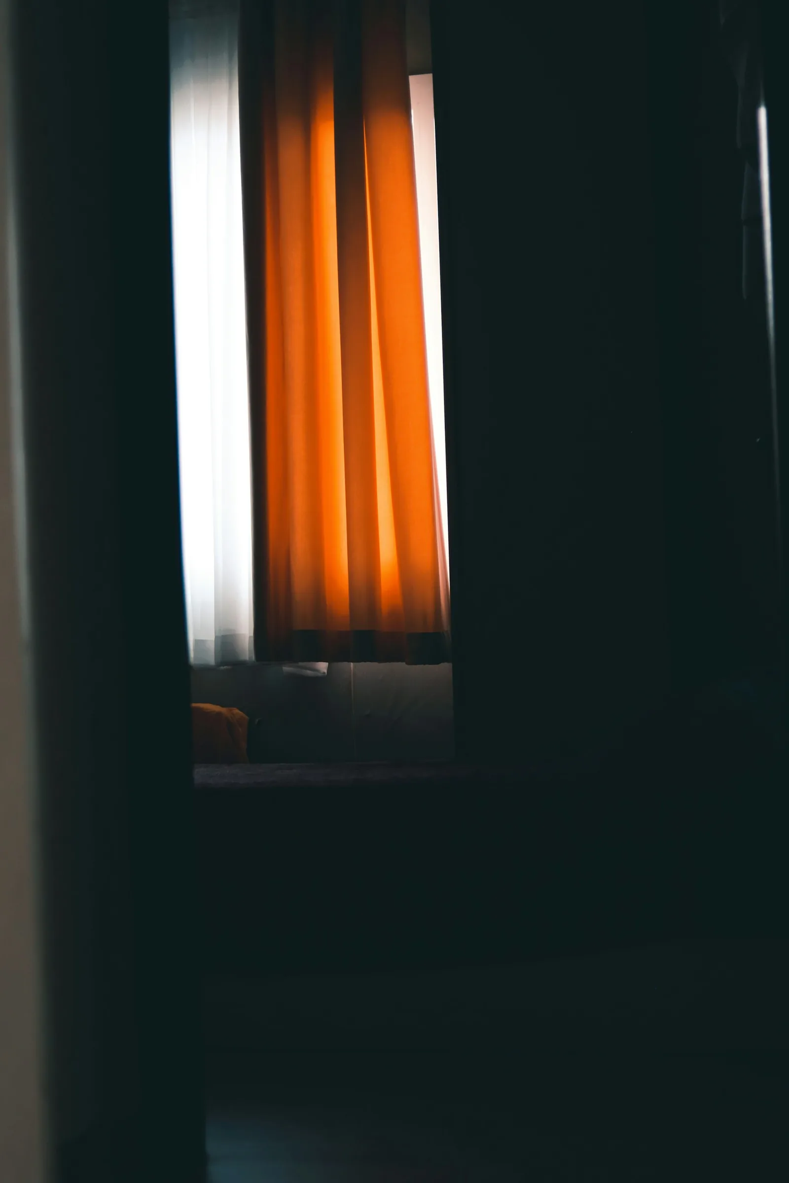A burnt-orange curtain lit from behind by daylight in an otherwise dark, deep-green room