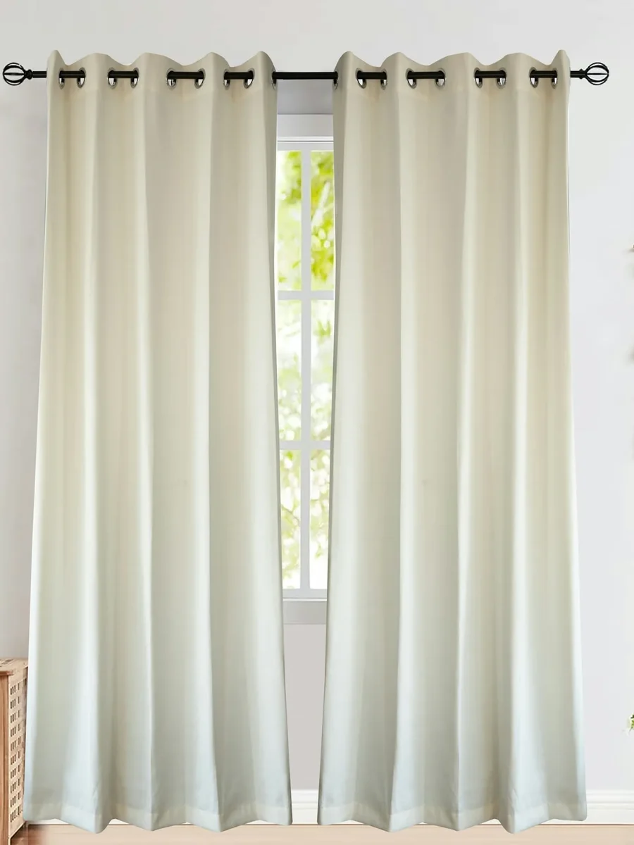 Cream eyelet curtains hung from a black rod over a window, with a side table and plant