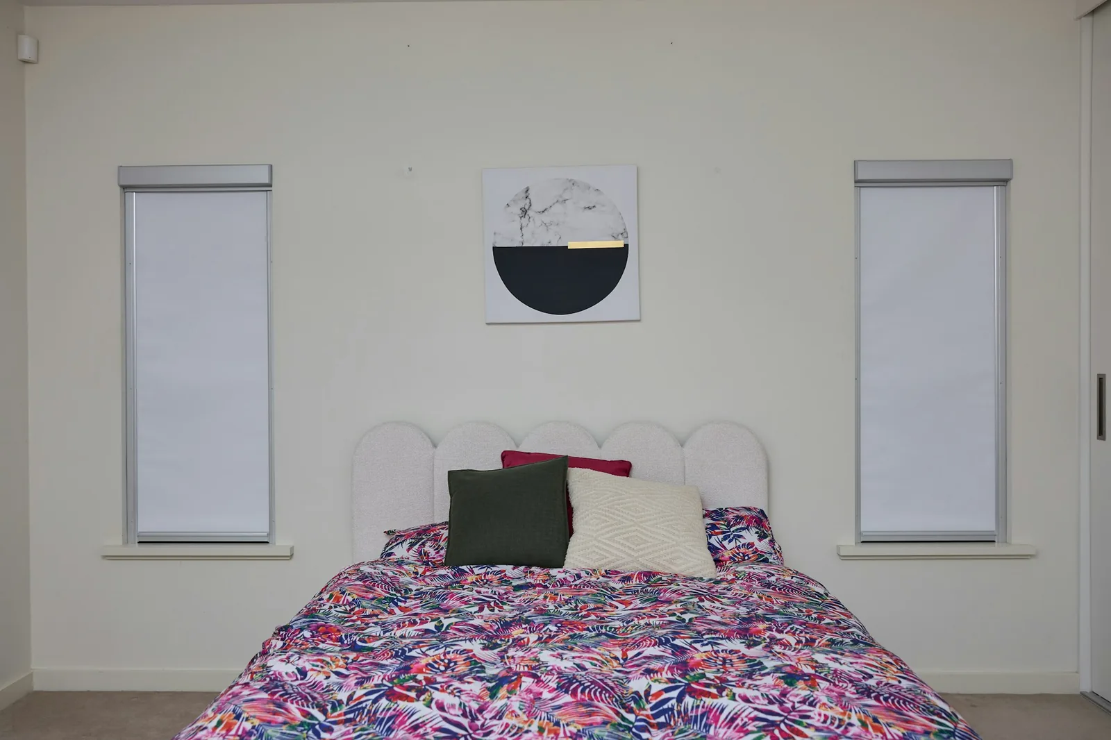 Two white fabric roller blinds pulled down on tall windows either side of a bed