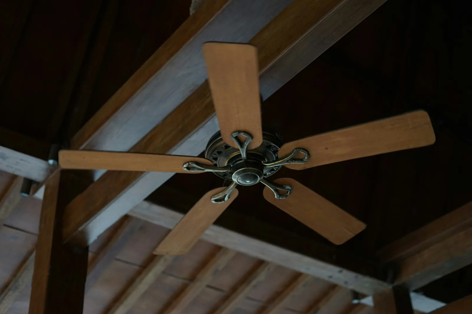 A wooden-bladed ceiling fan turning beneath an open timber-raftered roof