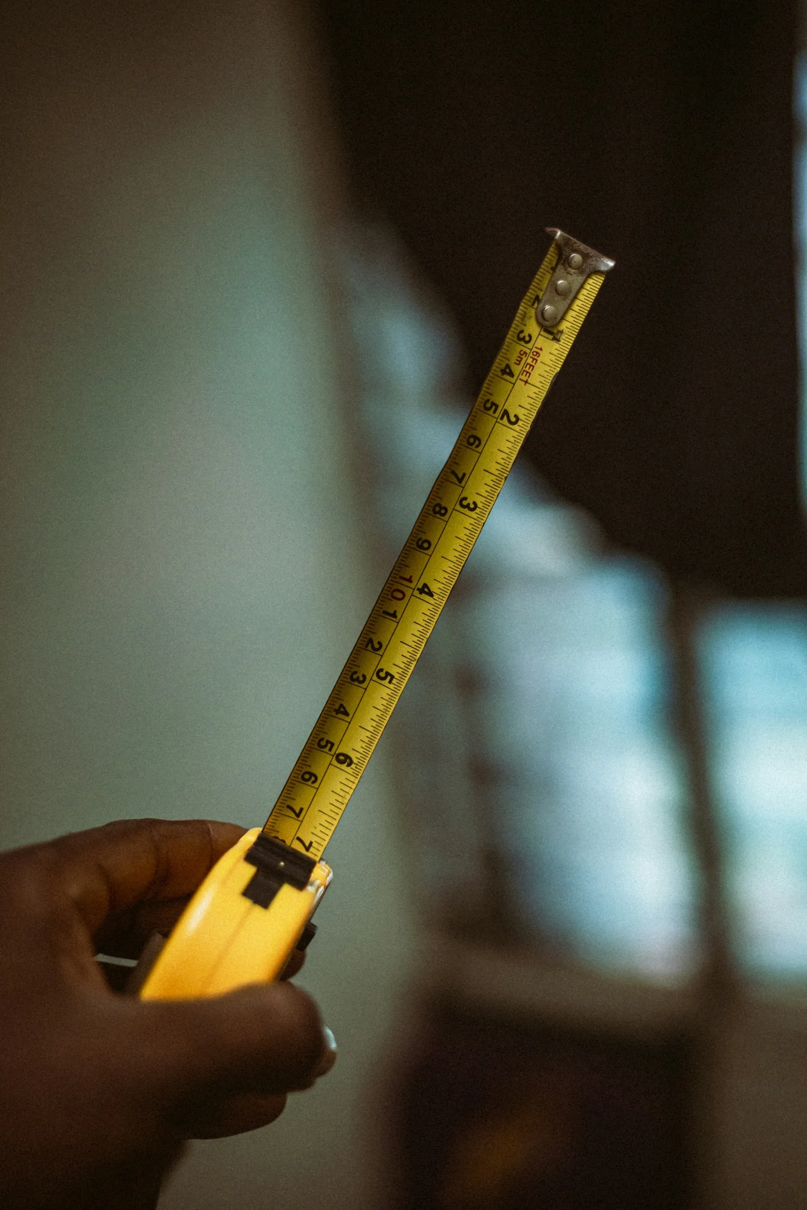 A hand extending a yellow tape measure in front of a window