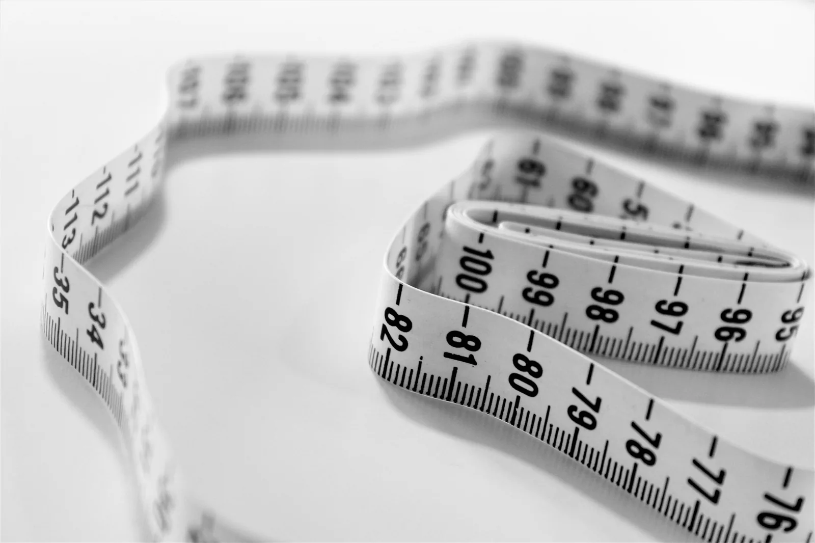 A cloth tape measure coiled loosely on a white surface, its centimetre markings in sharp focus