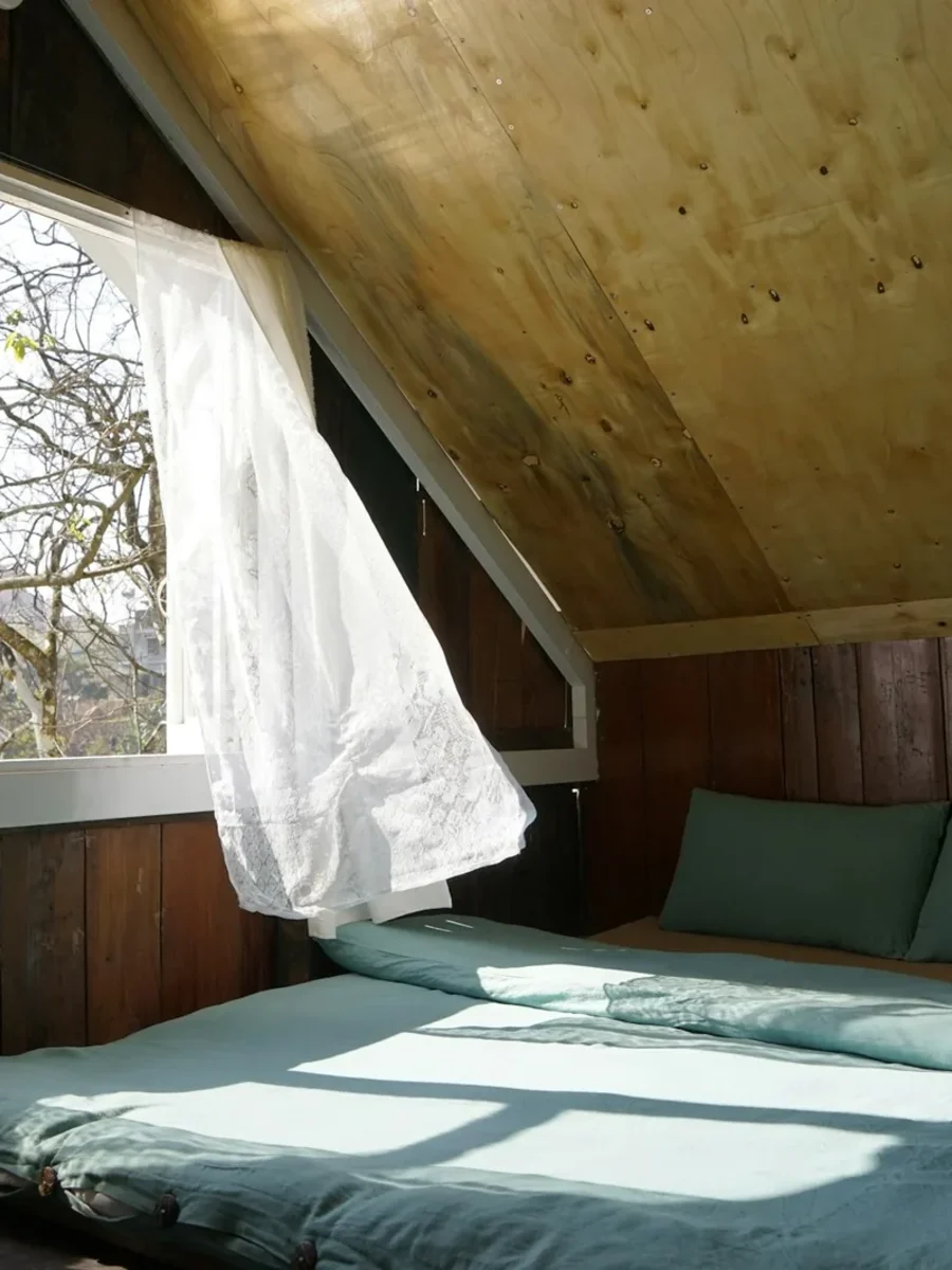 Sunlit attic bedroom with an open window and white curtains blowing inwards in the breeze