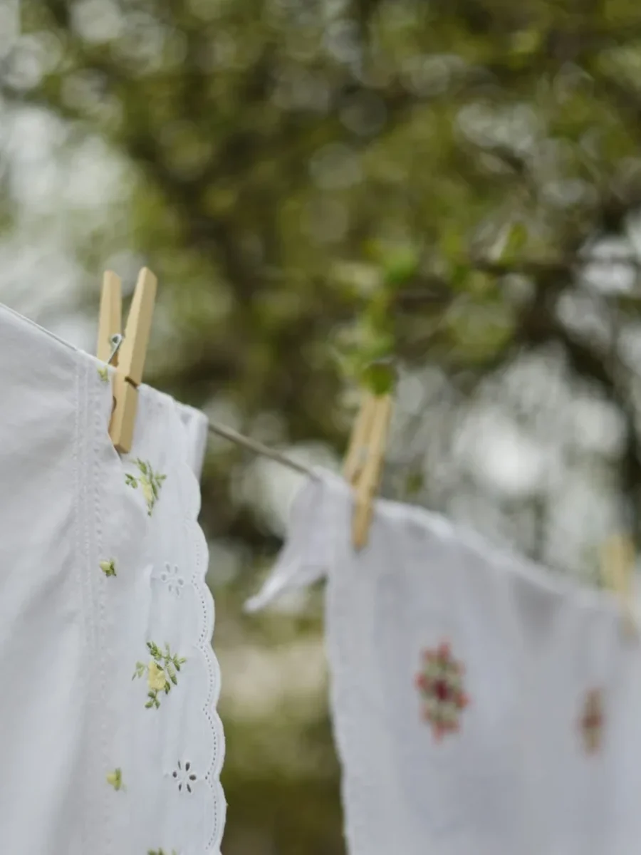 Embroidered white linens pegged on a clothesline outdoors, drying under a canopy of trees