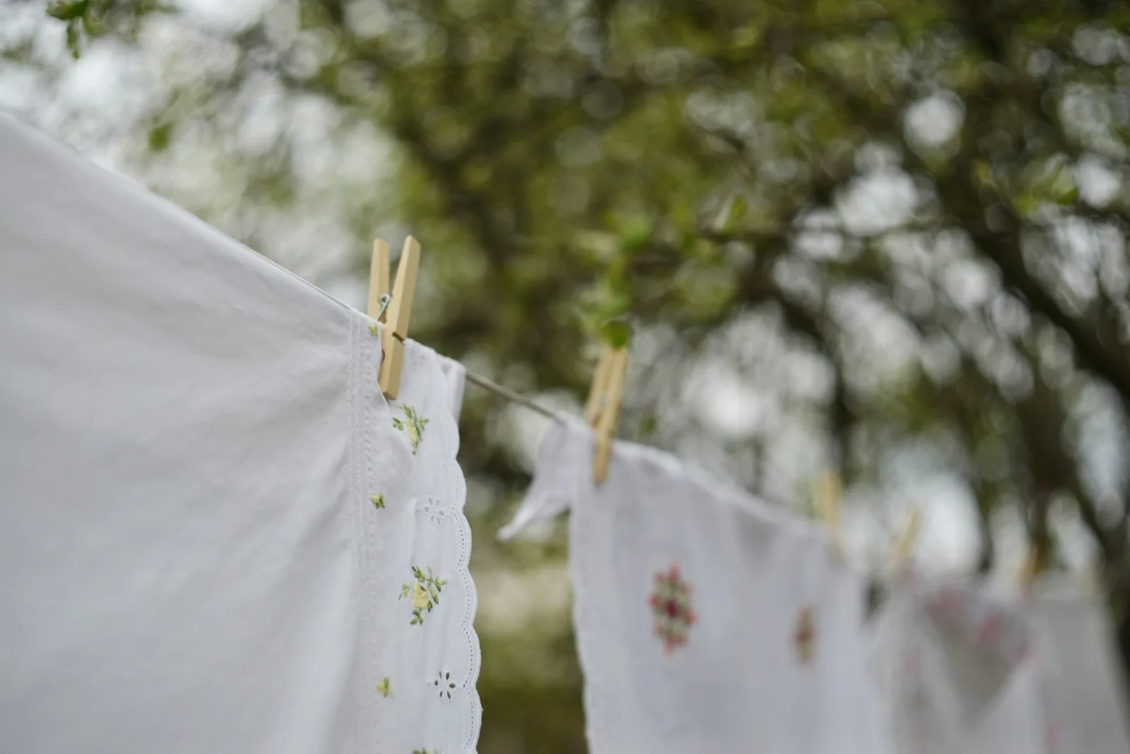 Embroidered white linens pegged on a clothesline outdoors, drying under a canopy of trees