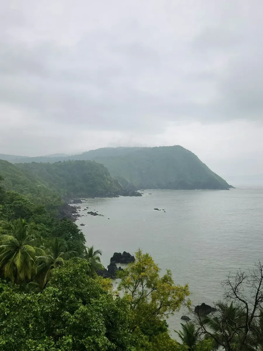 Misty monsoon sky over a green forested headland and a calm grey sea