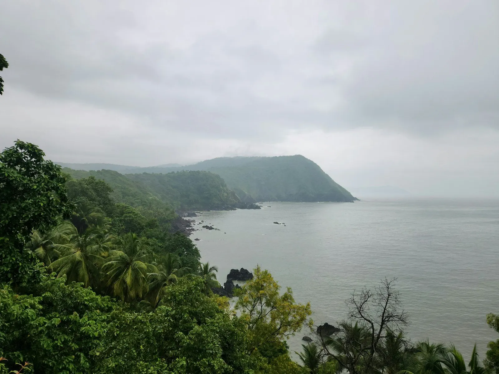 Misty monsoon sky over a green forested headland and a calm grey sea