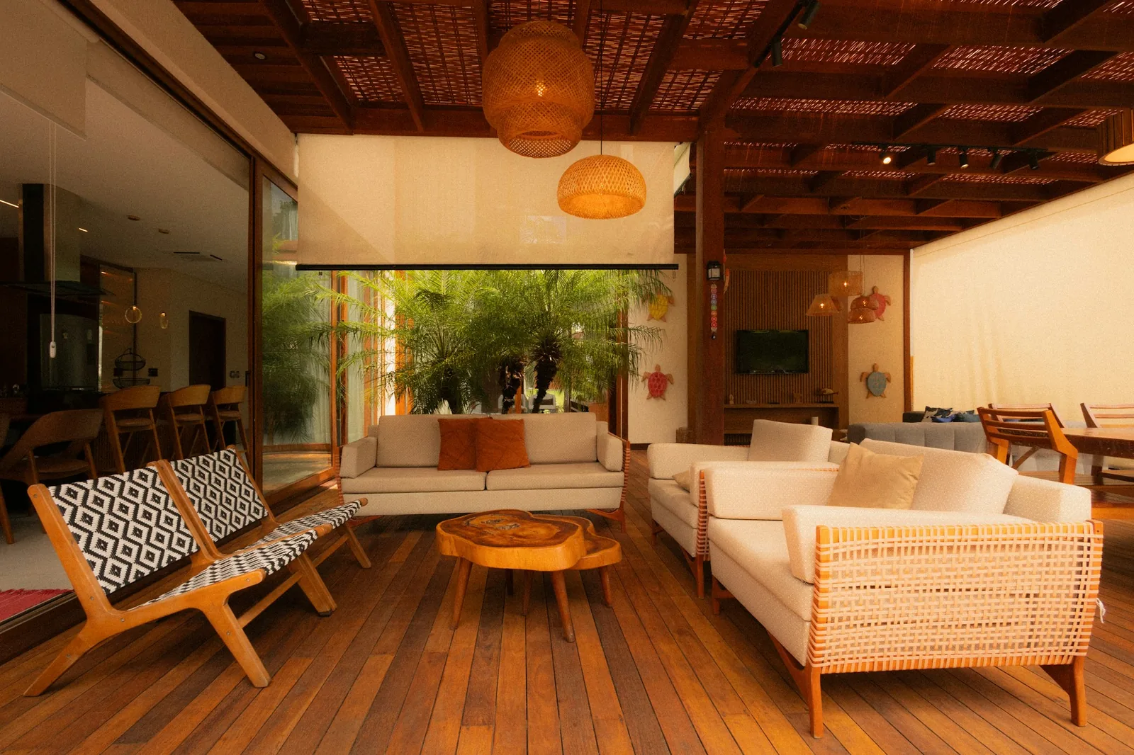 Covered timber-decked living veranda with white sofas, woven chairs, rattan lamps and a palm courtyard
