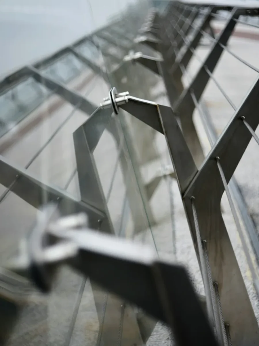 Close view of thin tensioned steel cables and angled posts on a glass-and-metal railing