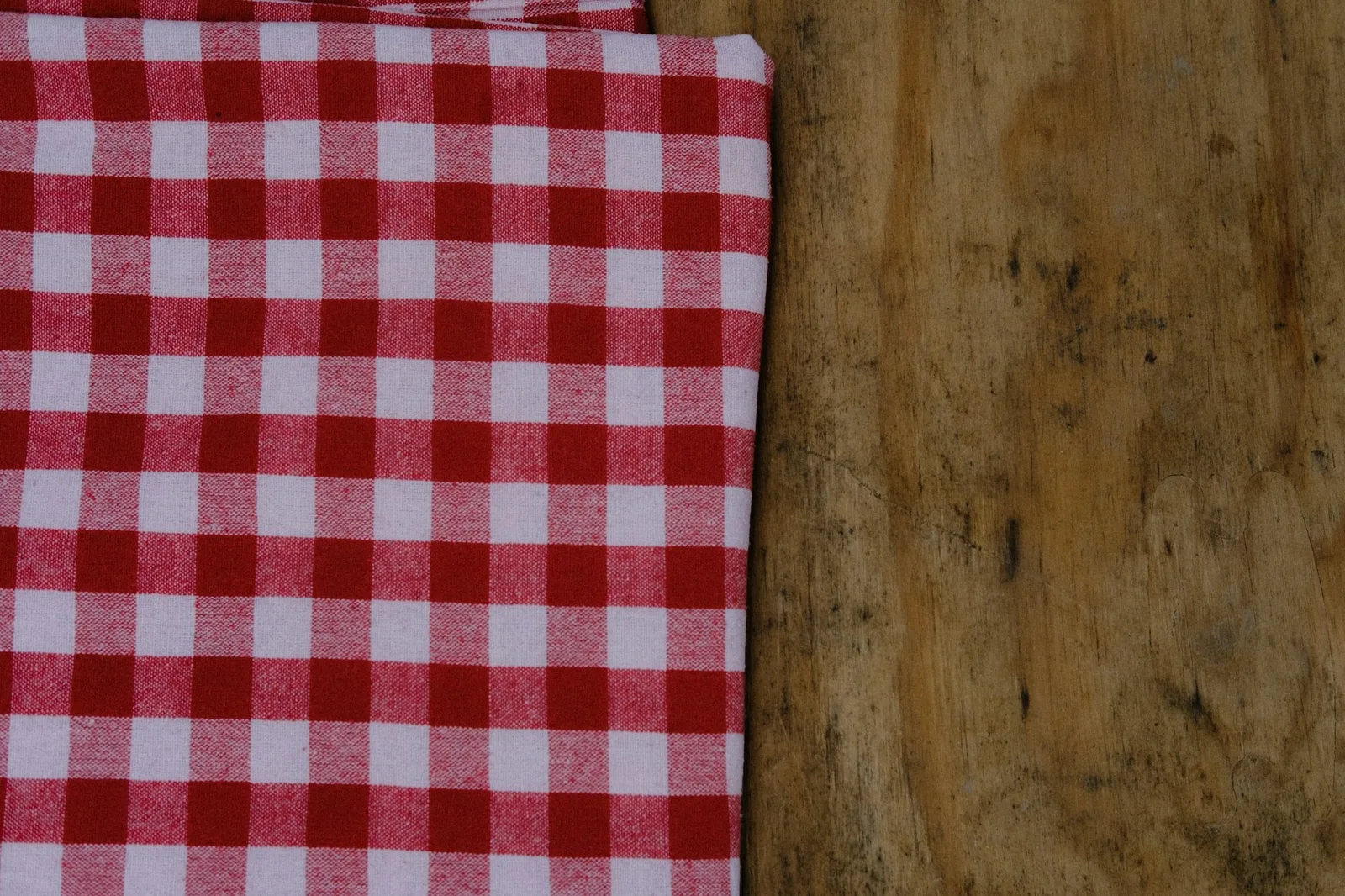 Folded red-and-white checked cotton cloth lying on a weathered wooden table
