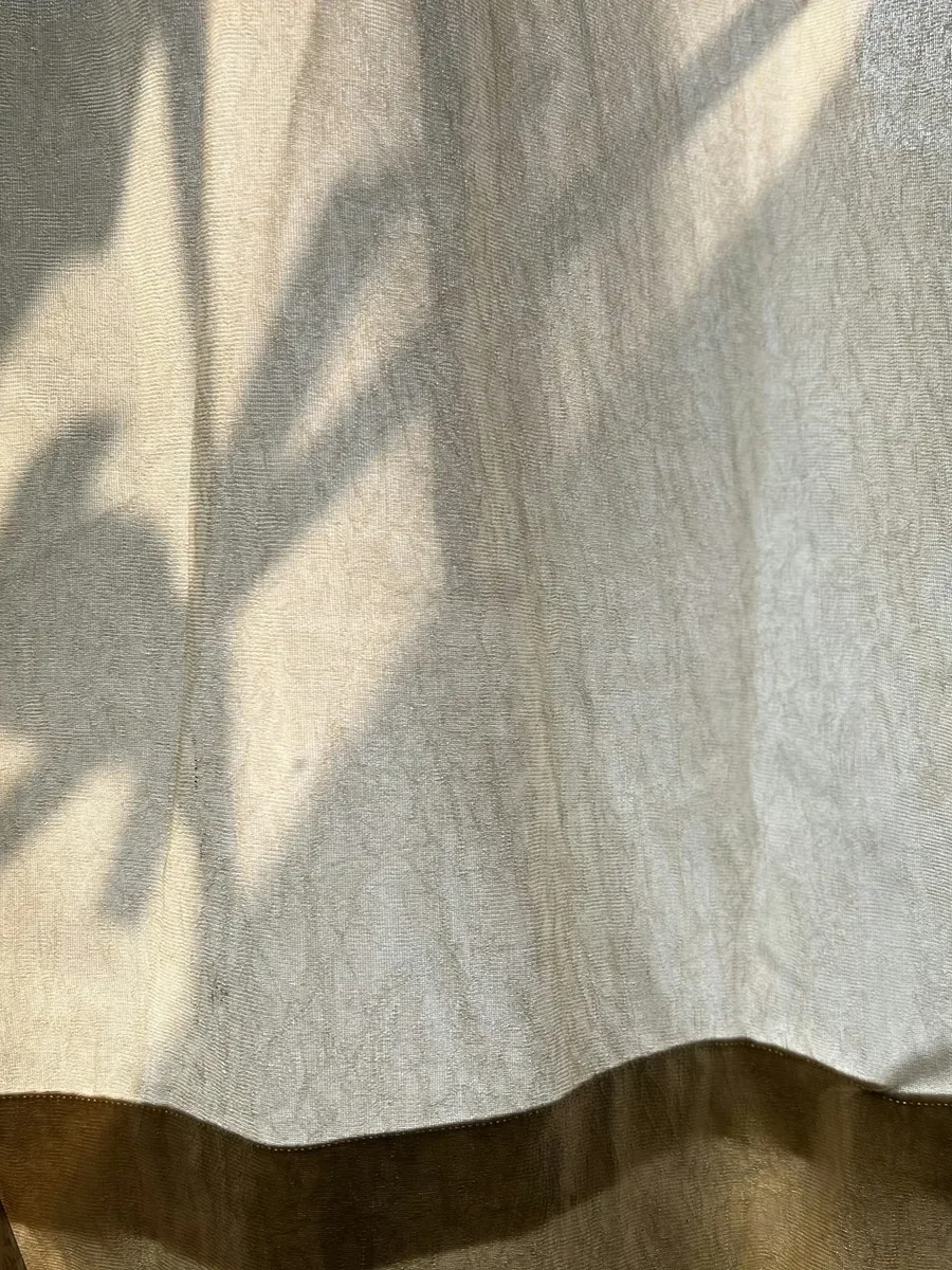 Sunlight casting a plant's shadow through a thin unlined curtain with a darker hem band