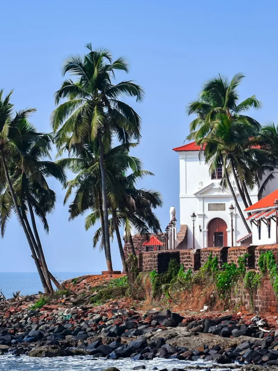 Whitewashed buildings with red-tiled roofs and coconut palms above a rocky stretch of tropical coastline