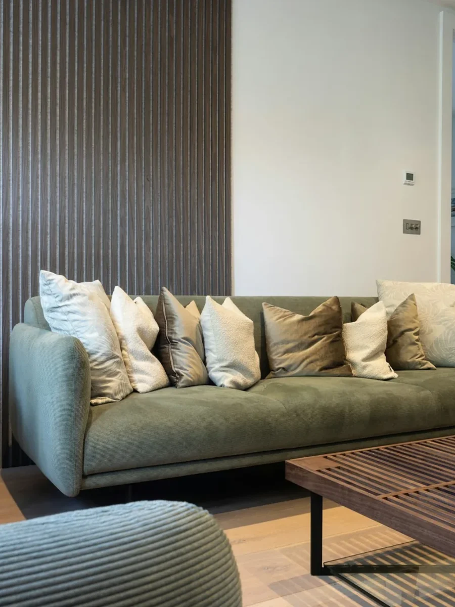 Dark fluted wood-slat feature wall behind a sage-green sofa piled with cushions