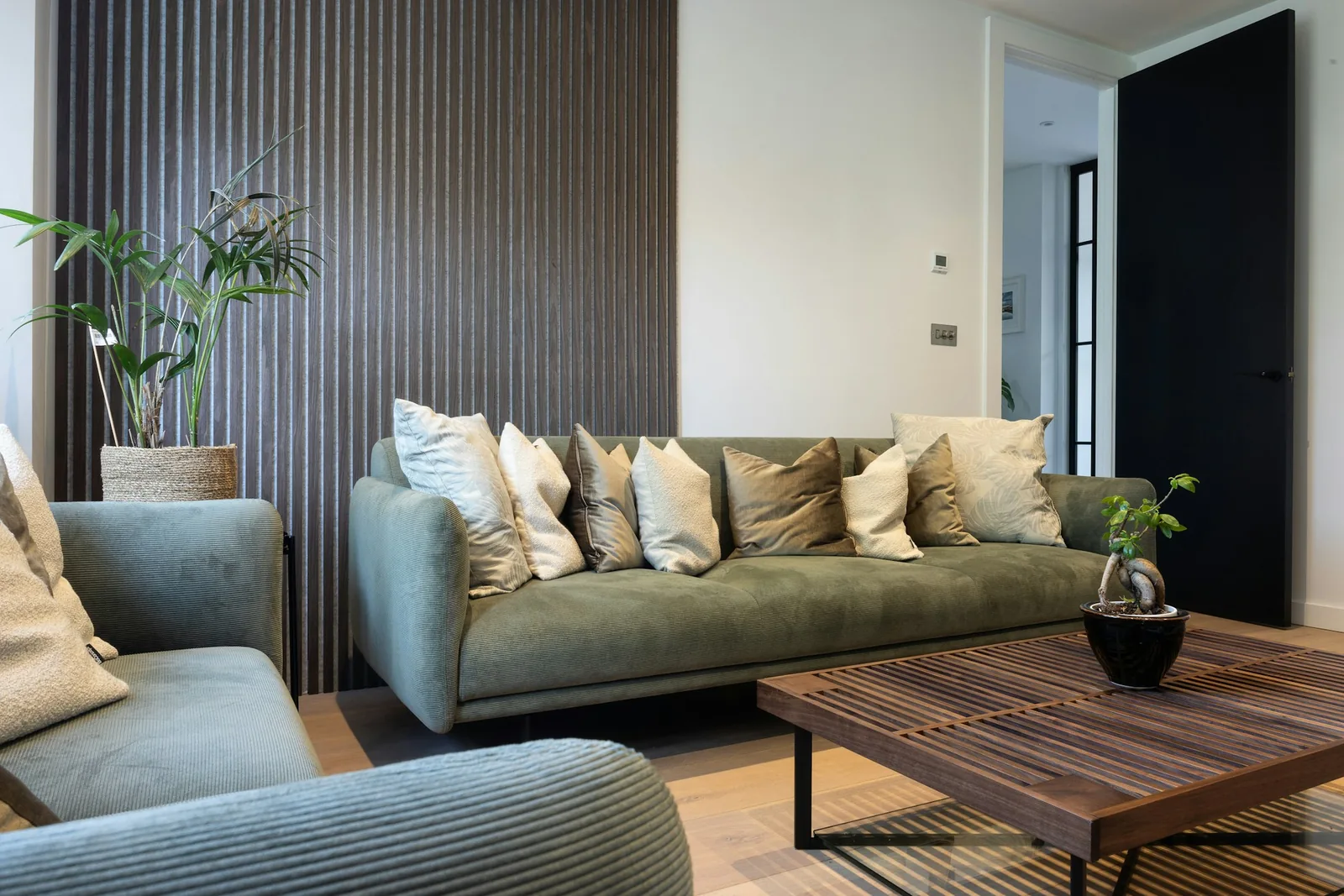 Dark fluted wood-slat feature wall behind a sage-green sofa piled with cushions