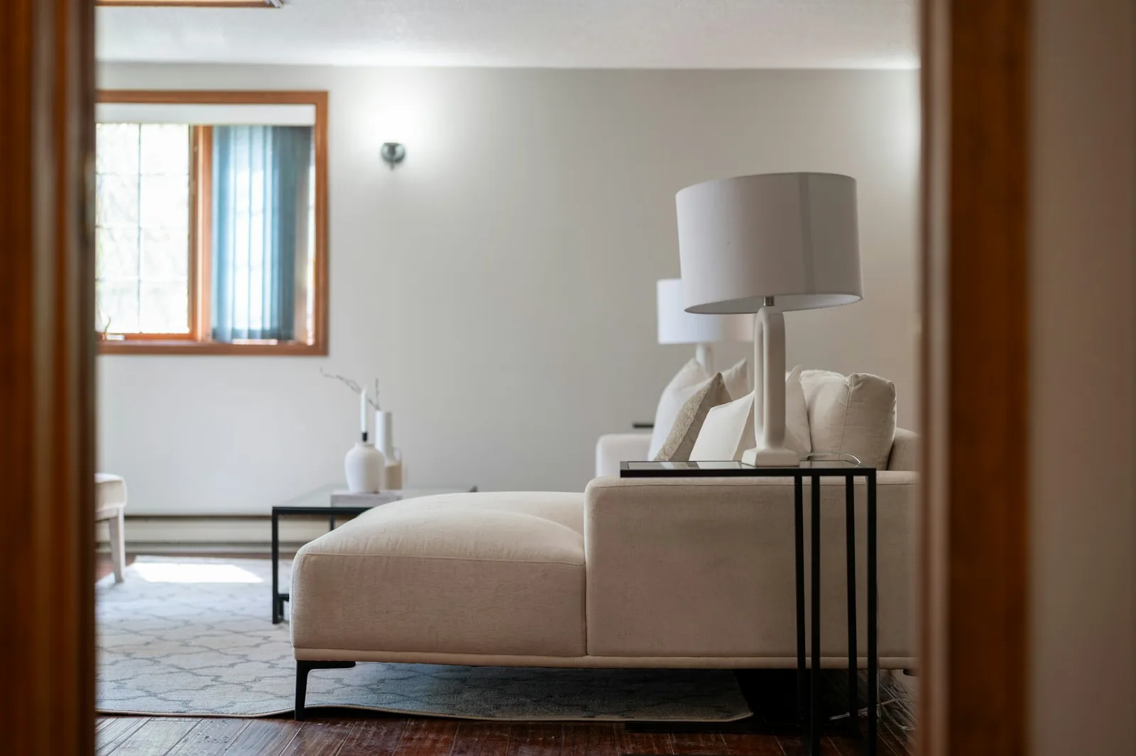 Cream chaise-ended lounge sofa with white lamps, glimpsed through a doorway into a living room