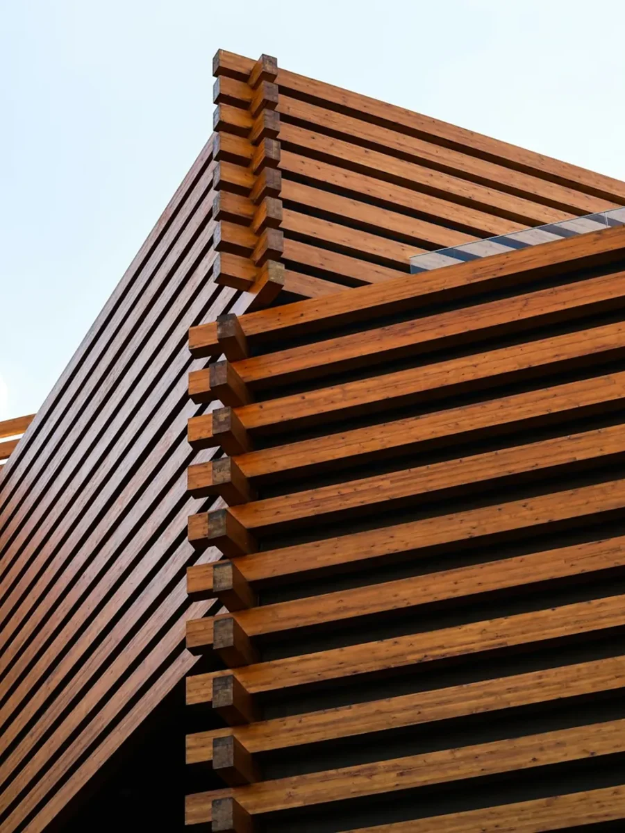 Exterior of a building wrapped in horizontal timber louvre slats against a pale sky
