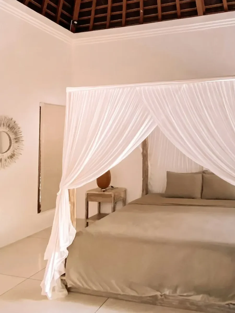 Serene bedroom with a white-draped four-poster bed beneath an exposed timber roof