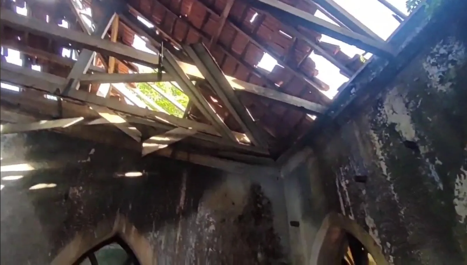 Broken clay roof tiles and exposed timber rafters letting daylight into an abandoned Goan house