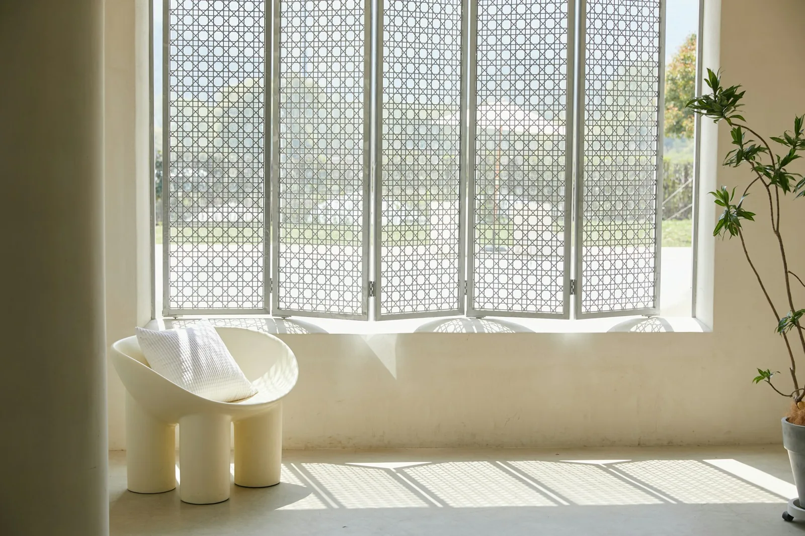 Minimal cream room with a single sculptural chair before a window of white lattice screens