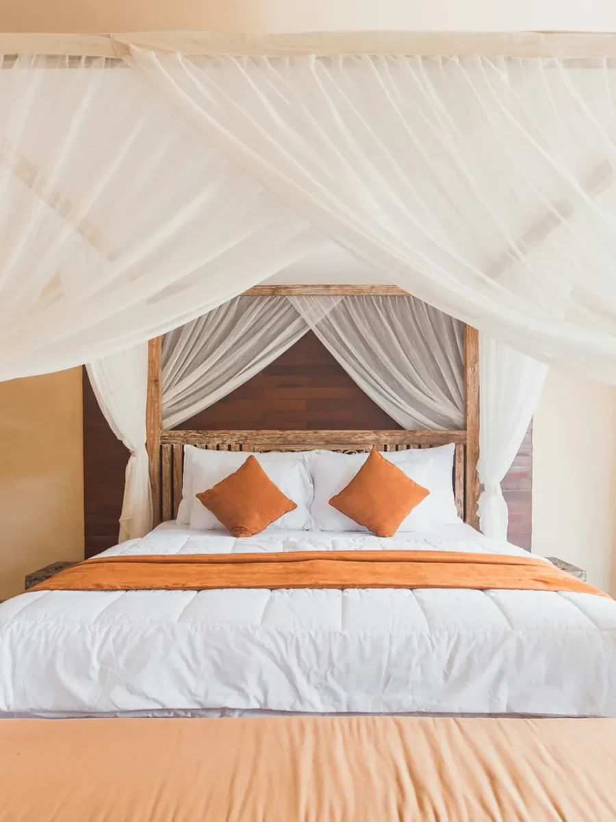 Four-poster bed draped with a white mosquito net tied back at each post in a tropical room