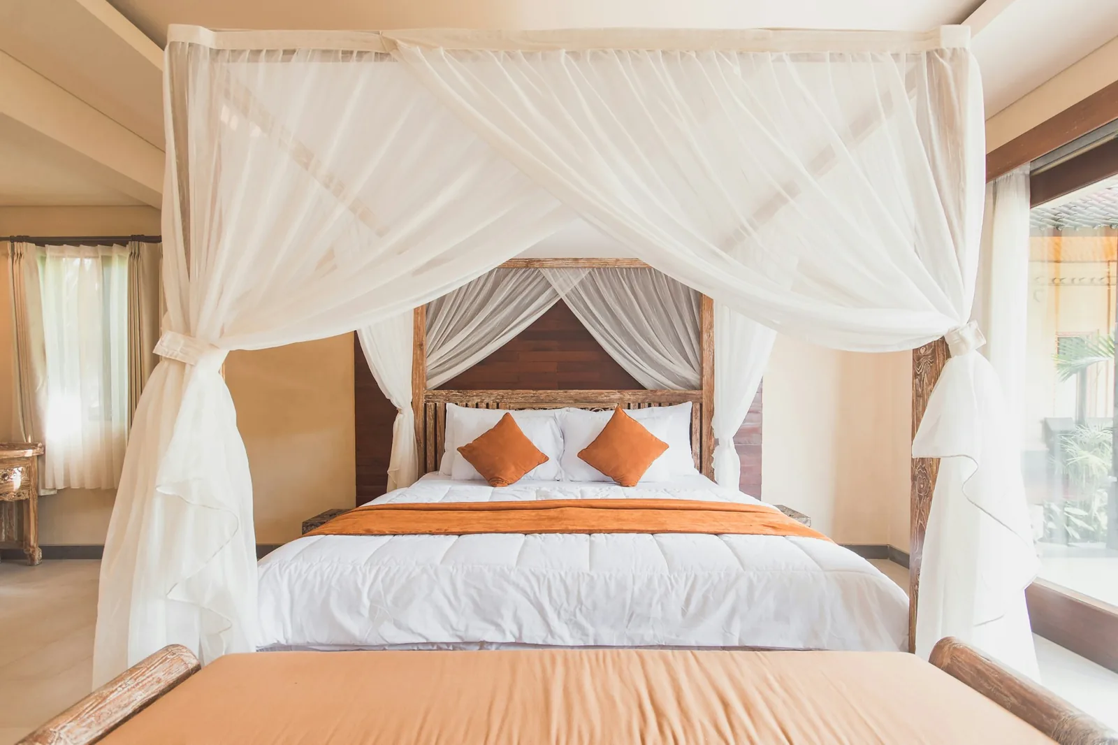 Four-poster bed draped with a white mosquito net tied back at each post in a tropical room