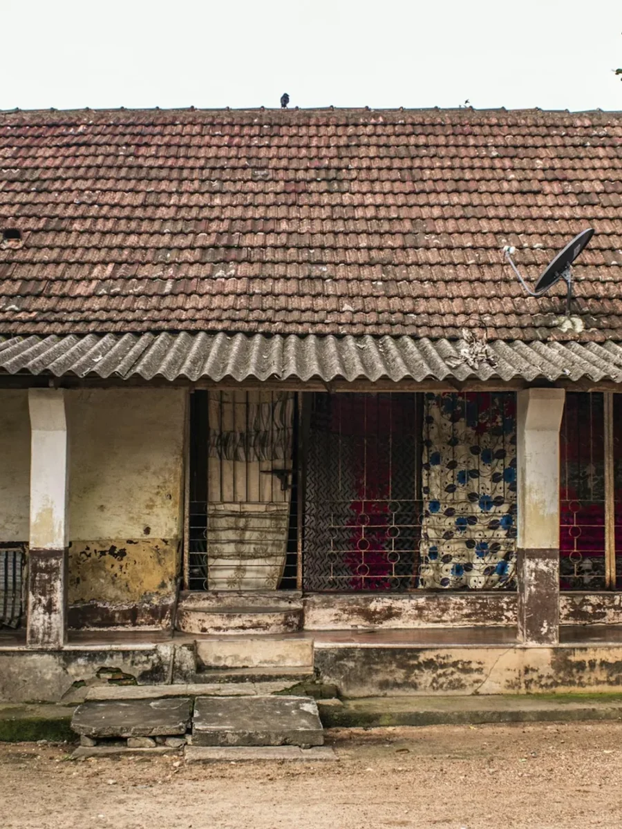 Weathered single-storey Indian house with a clay-tiled roof, grilled verandah and patterned cloth screens