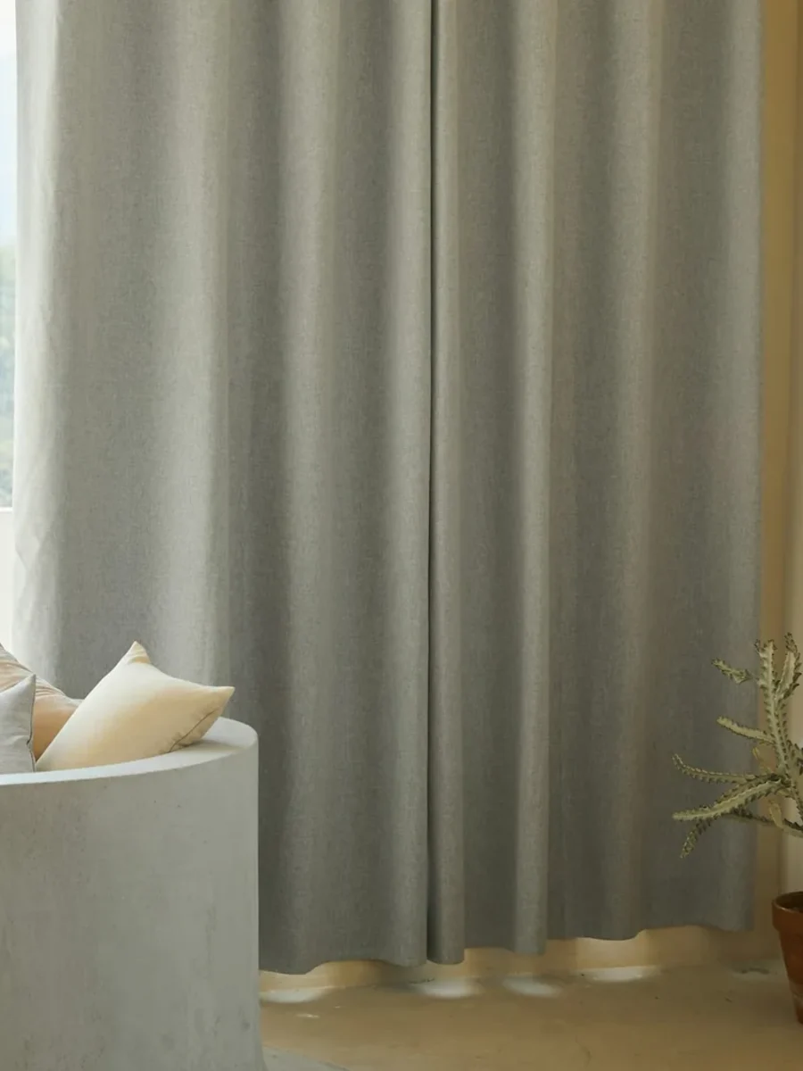 Heavy grey full-length curtain drawn beside a window, with a curved built-in seat and cushions