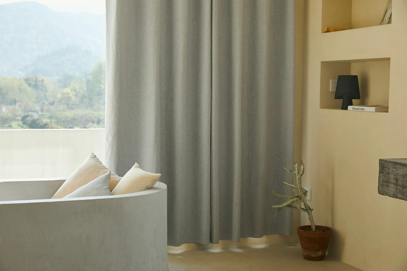 Heavy grey full-length curtain drawn beside a window, with a curved built-in seat and cushions