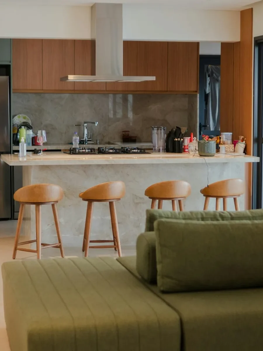 An open kitchen with island and bar stools flowing into a living area with an olive-green sofa