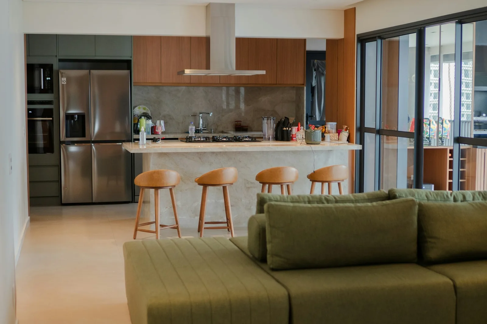 An open kitchen with island and bar stools flowing into a living area with an olive-green sofa