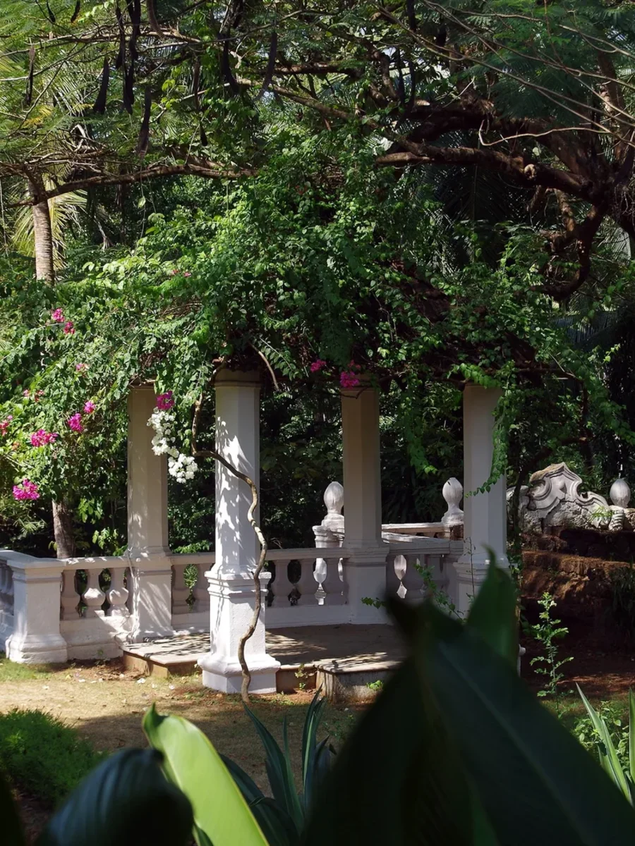 The garden of the Palácio do Deão in Quepem, with white pillared balustrades under bougainvillea and palms