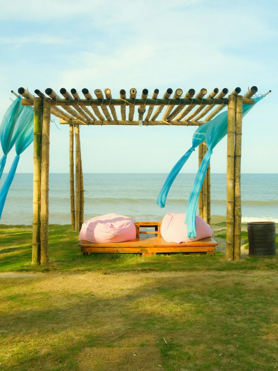 A bamboo pergola draped with flowing turquoise fabric over a low daybed on a lawn facing the sea