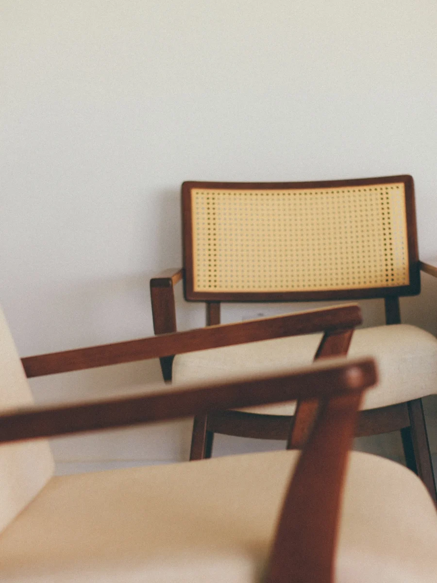 A low lounge chair with a cane-woven back, cushioned seat and long wooden armrests against a white wall