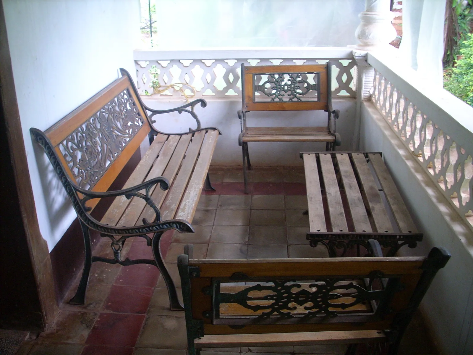 A shaded Goan verandah with cast-iron and timber benches against a pierced white balustrade