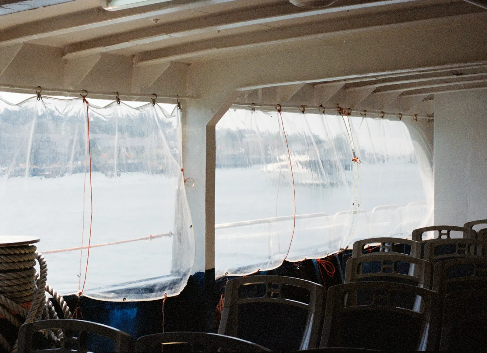 Clear plastic roll-down curtains tied along the open side of a covered deck above water