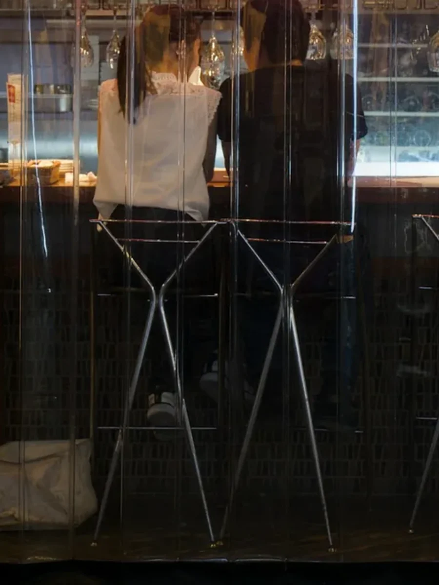 Clear PVC curtain panels enclosing a restaurant counter, with two diners seen from behind on bar stools