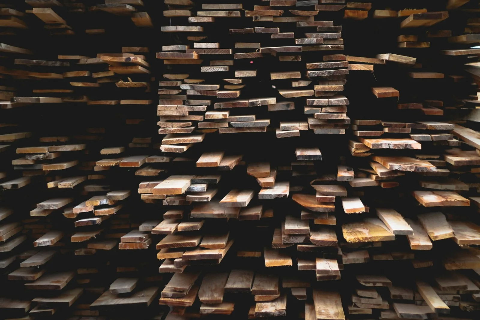 A deep stack of rough-sawn timber planks with weathered ends seen head-on