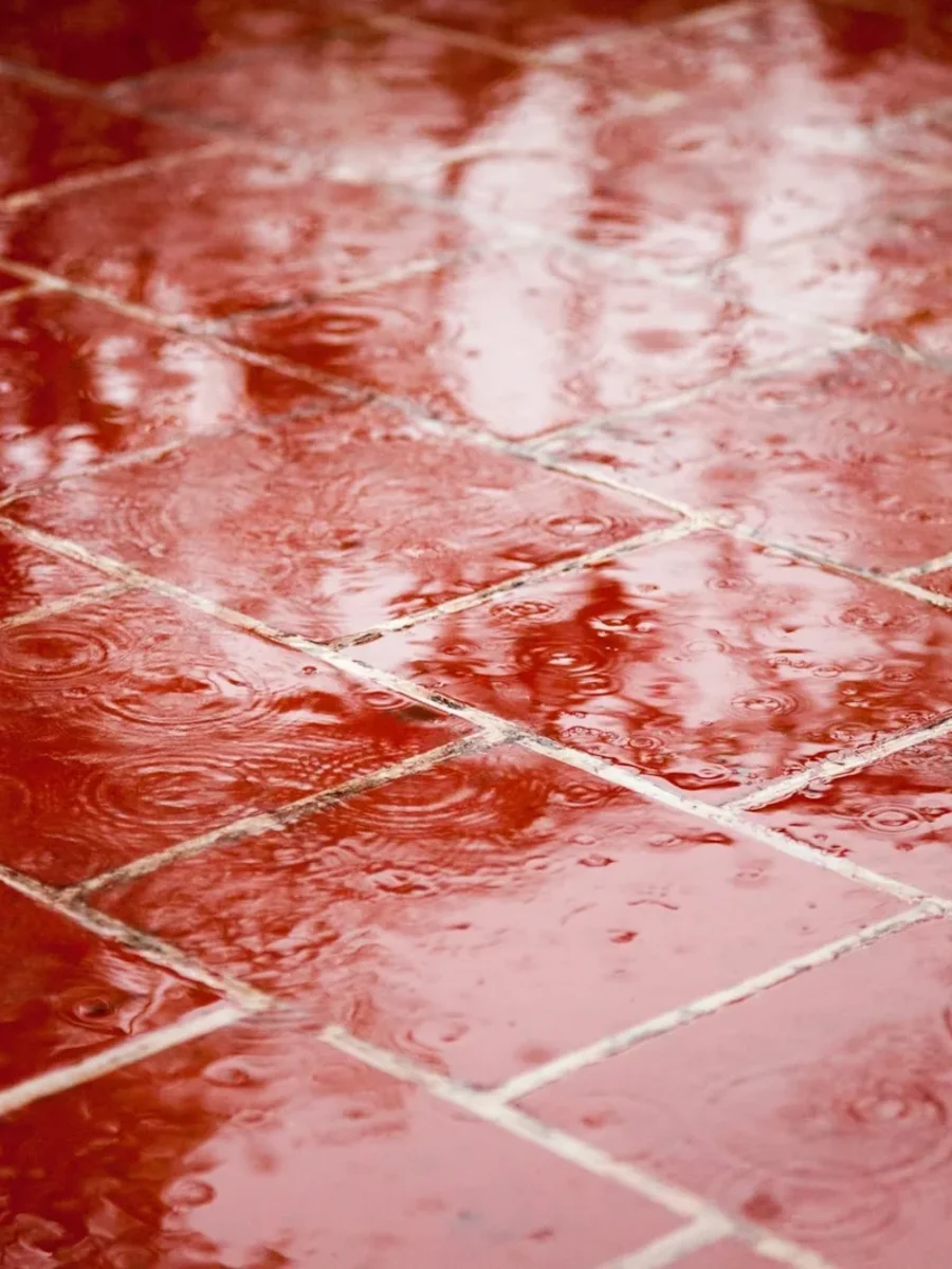 Glossy red square floor tiles wet with rain, reflecting the light in rippled puddles