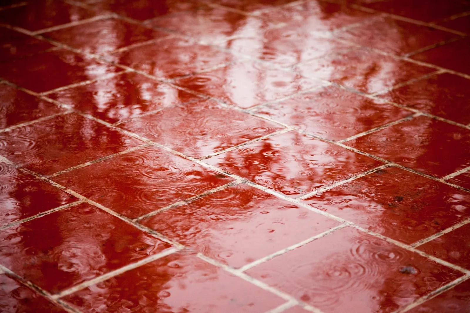 Glossy red square floor tiles wet with rain, reflecting the light in rippled puddles