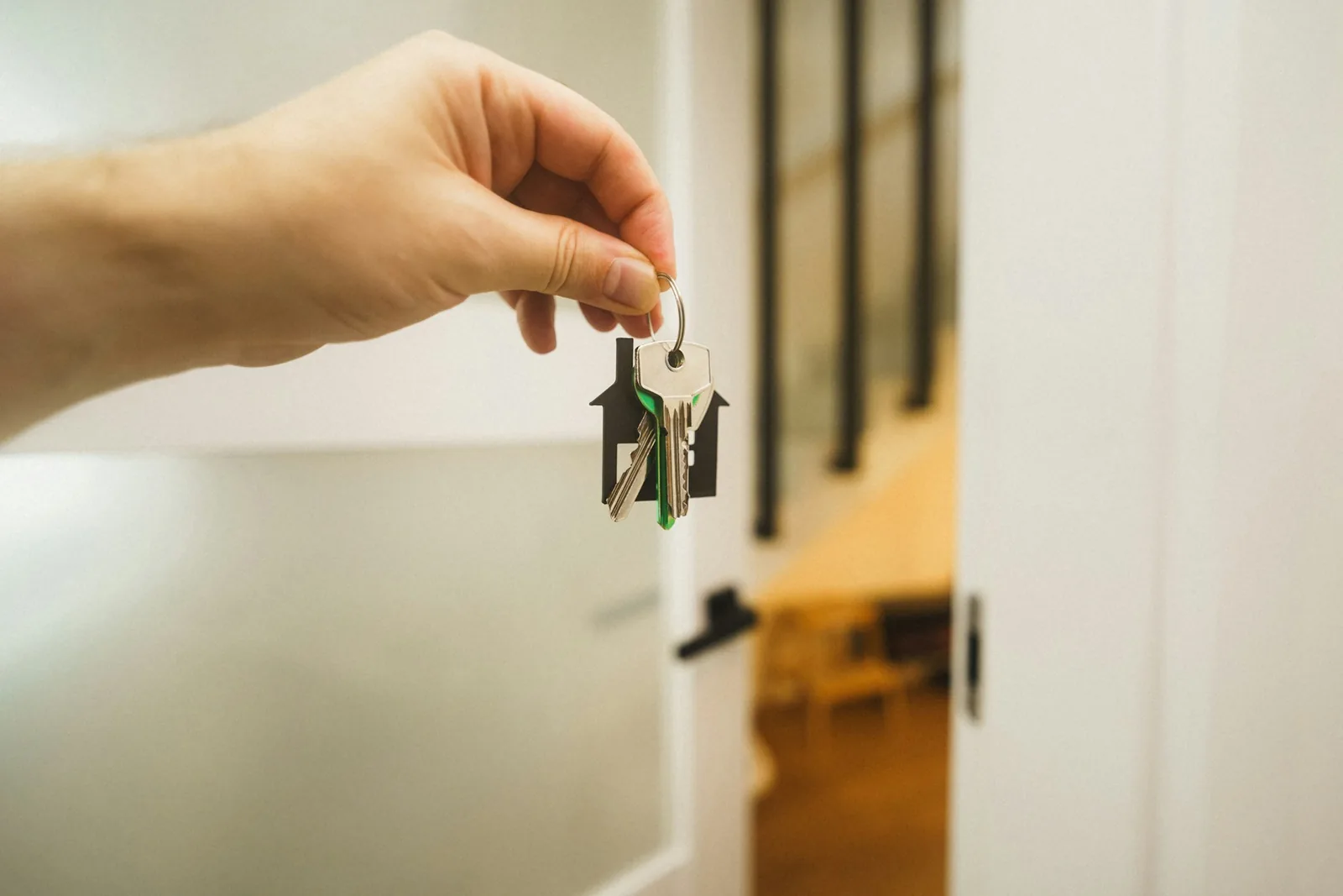 A hand holding a set of house keys on a house-shaped keyring beside an open white door