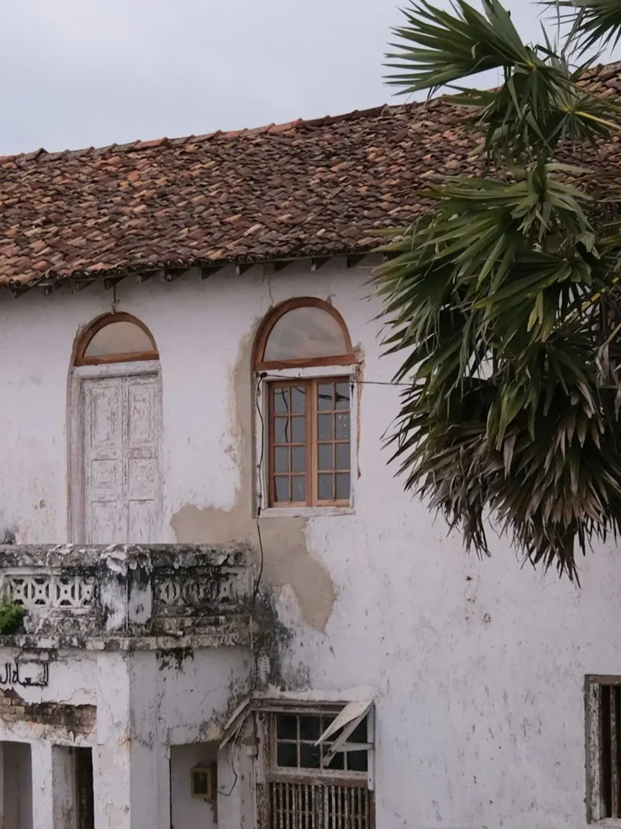Weathered whitewashed colonial house with arched windows, a tiled roof and a crumbling balcony