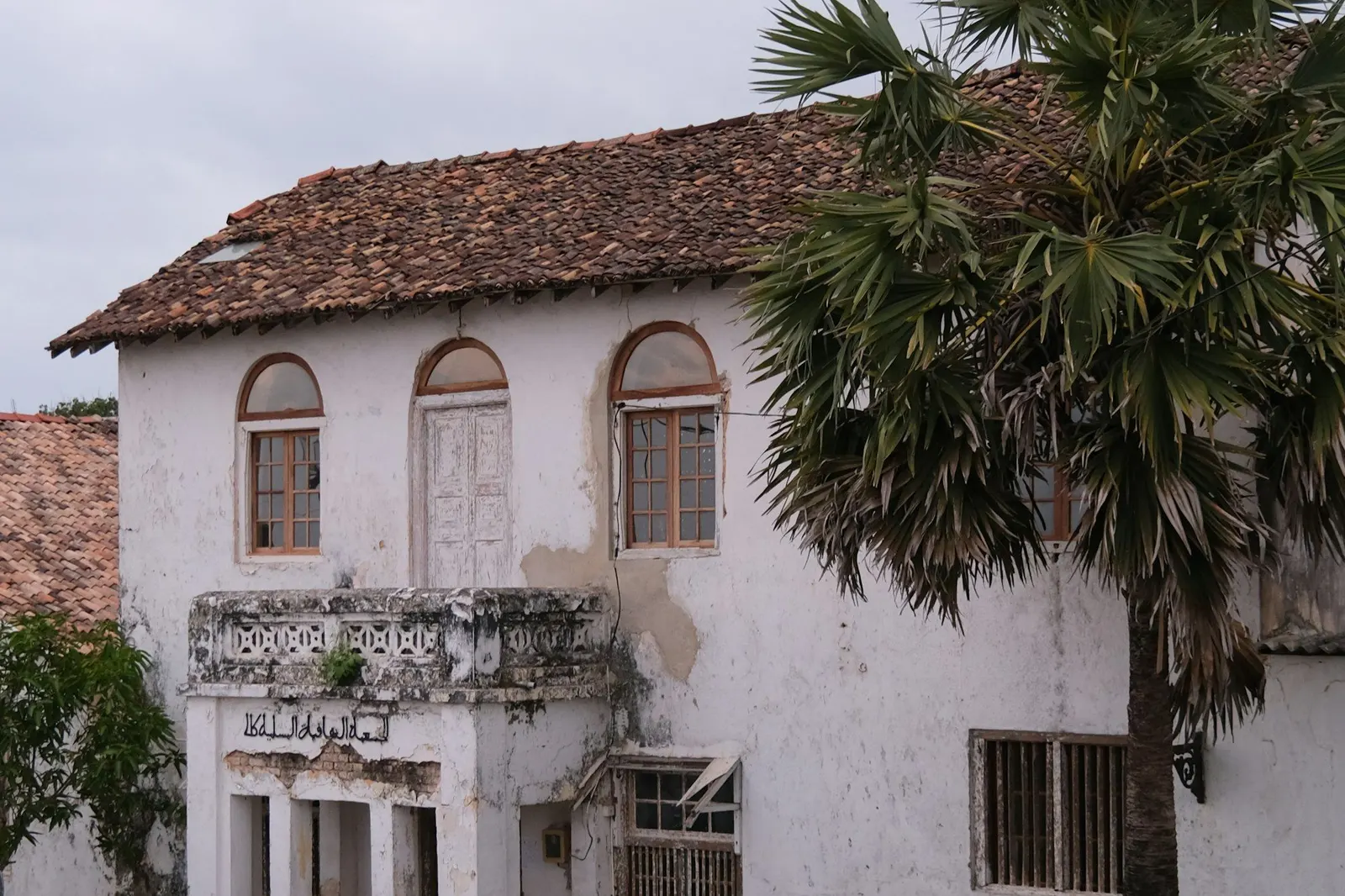 Weathered whitewashed colonial house with arched windows, a tiled roof and a crumbling balcony