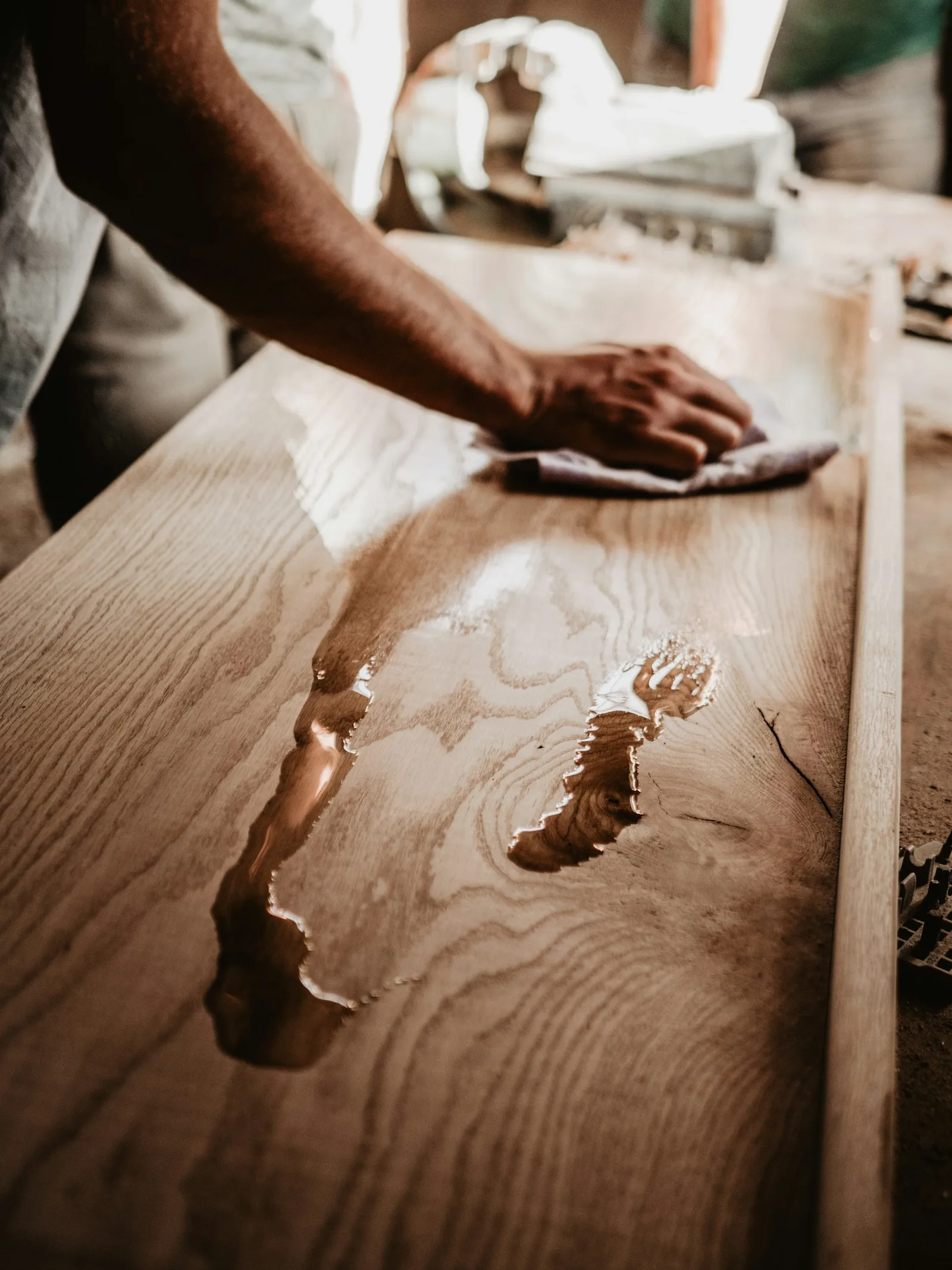 A craftsman wiping oil onto a pale oak tabletop with a cloth, showing the grain darkening