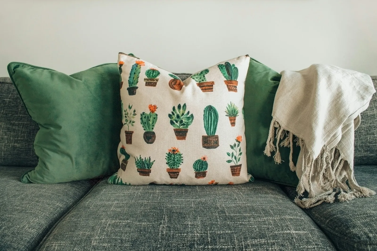 Green velvet and cactus-print cushions with a fringed linen throw on a grey textured sofa