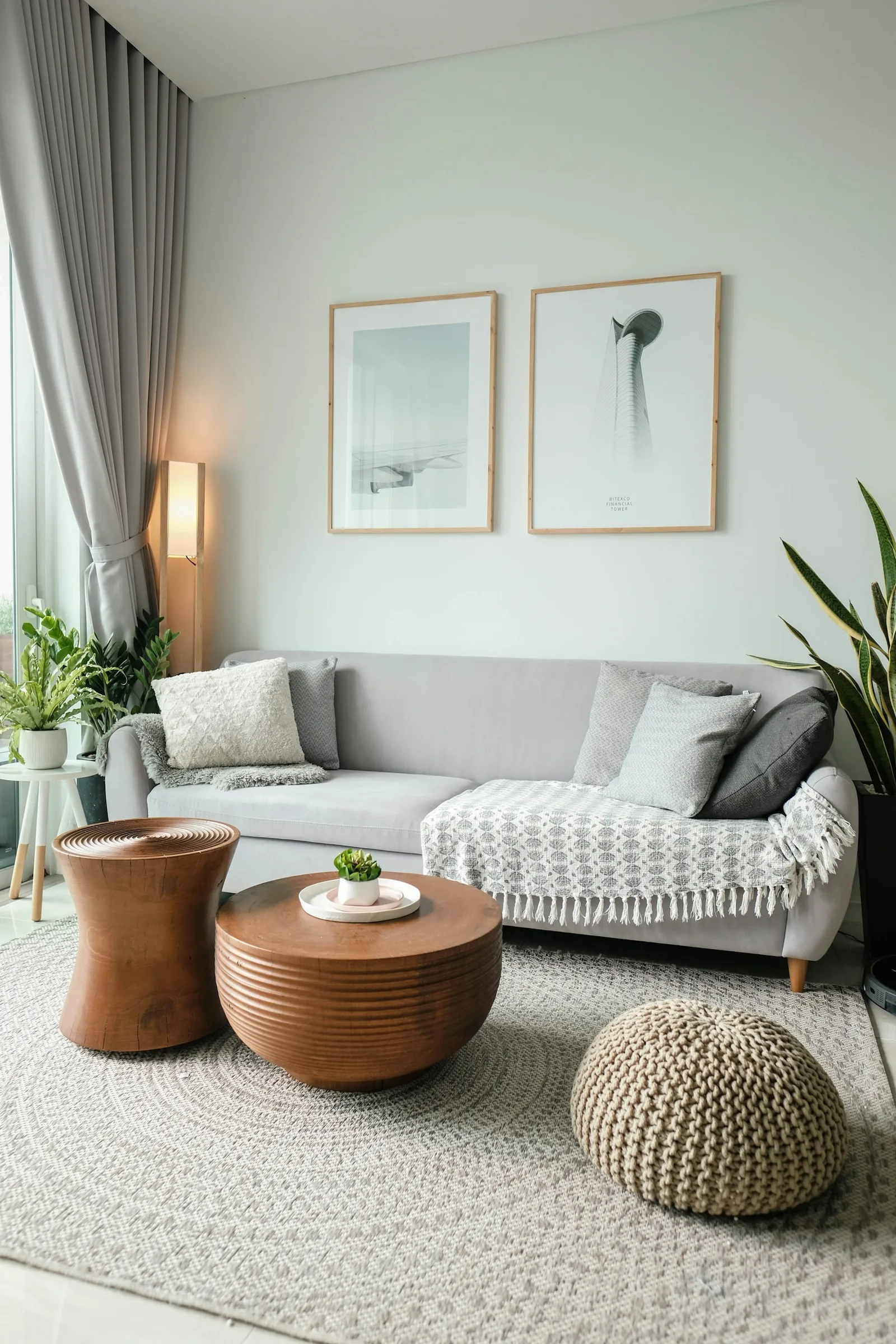 A grey sofa, wooden side tables and a knitted pouf arranged on a large round textured rug